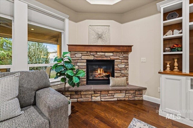 living area with a stone fireplace, hardwood / wood-style flooring, and baseboards