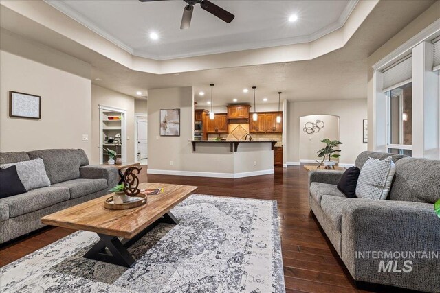 living area featuring dark wood-style floors, baseboards, a tray ceiling, and ornamental molding