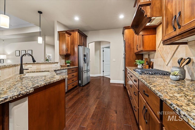 kitchen with brown cabinetry, arched walkways, a sink, stainless steel appliances, and dark wood-type flooring