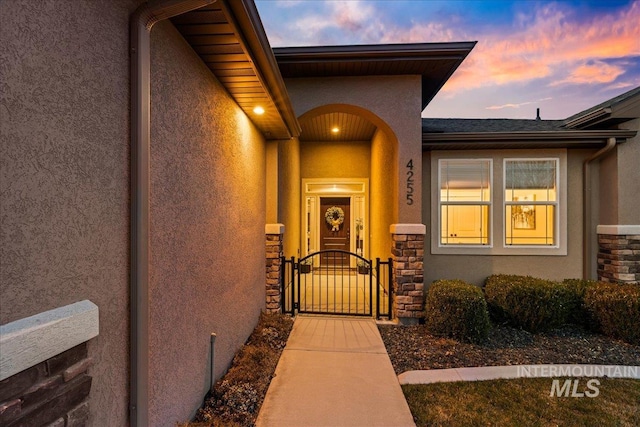 entrance to property featuring stone siding, stucco siding, and a gate