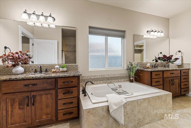 bathroom with a sink, backsplash, two vanities, and a bath