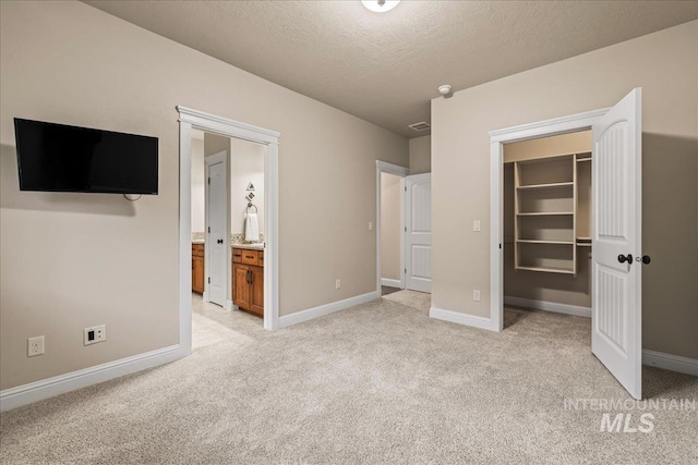 unfurnished bedroom featuring baseboards, light colored carpet, a spacious closet, and a textured ceiling