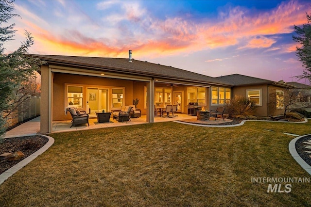 back of house at dusk with stucco siding, a fire pit, a lawn, and a patio area