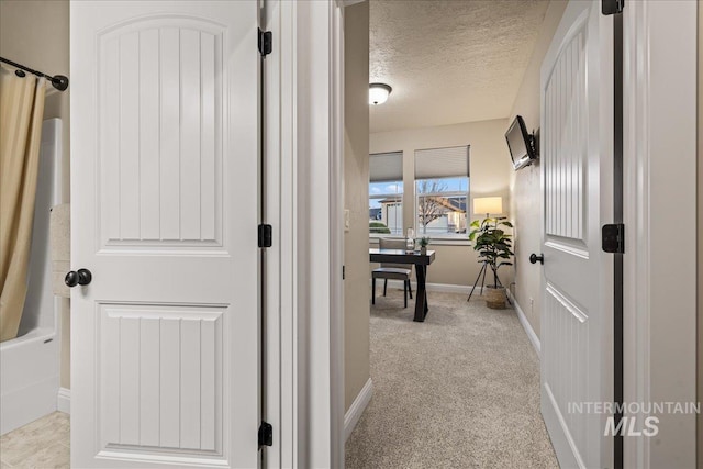 hallway featuring light carpet, a textured ceiling, and baseboards