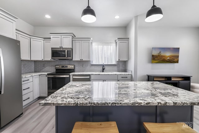 kitchen with a sink, stainless steel appliances, decorative backsplash, a center island, and light wood-style floors