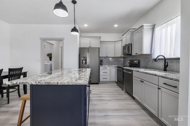 kitchen featuring a sink, stainless steel appliances, decorative backsplash, light stone countertops, and a kitchen island