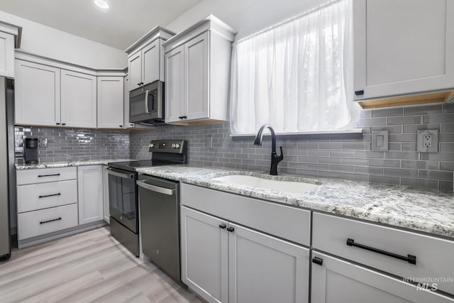 kitchen featuring light wood-style floors, decorative backsplash, appliances with stainless steel finishes, and a sink