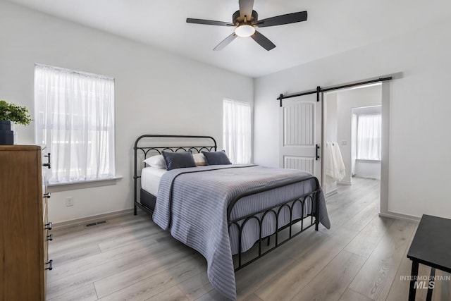 bedroom featuring baseboards, a barn door, light wood-type flooring, and visible vents