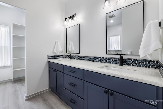 bathroom with a sink, double vanity, baseboards, and wood finished floors