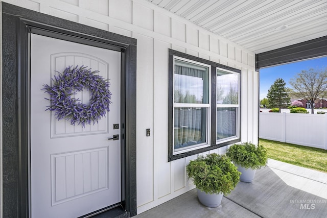 doorway to property with board and batten siding, a porch, and fence