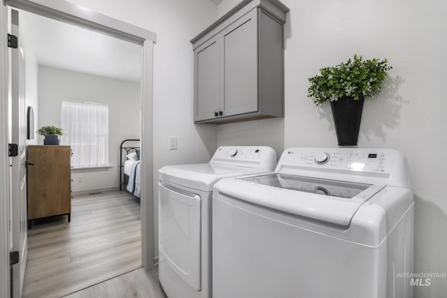 laundry room featuring washing machine and clothes dryer, light wood-style flooring, and cabinet space