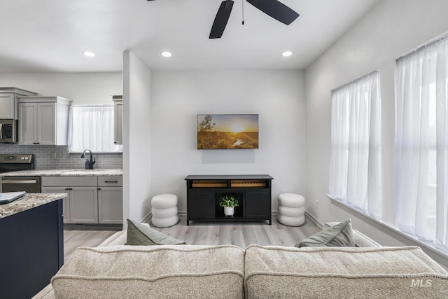 living room featuring light wood-type flooring, baseboards, a ceiling fan, and recessed lighting