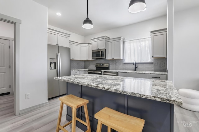 kitchen with light wood finished floors, appliances with stainless steel finishes, tasteful backsplash, and a kitchen bar
