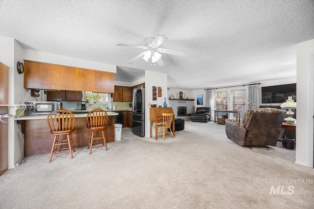 kitchen with stainless steel refrigerator, a kitchen breakfast bar, light carpet, a brick fireplace, and kitchen peninsula