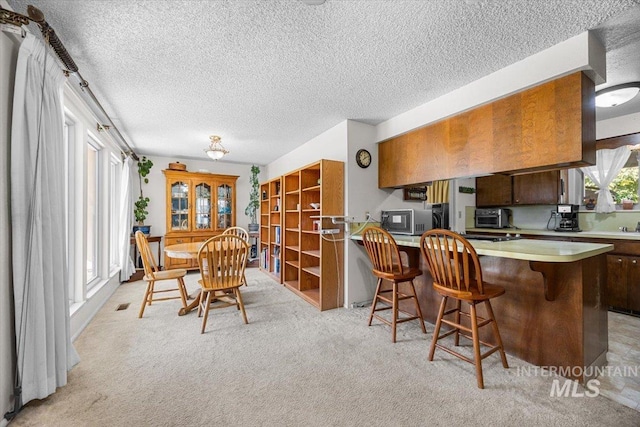 kitchen featuring light carpet, a breakfast bar area, a textured ceiling, and kitchen peninsula