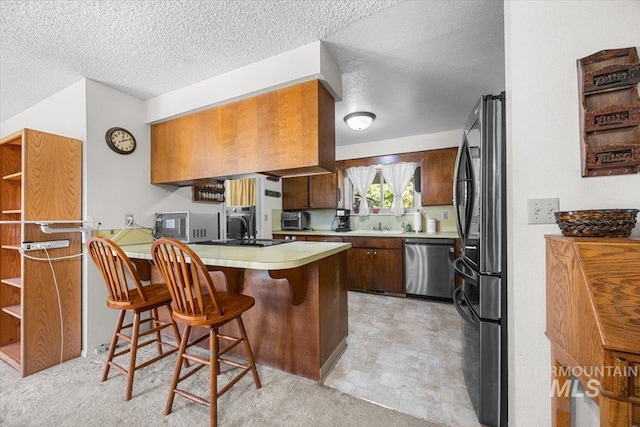 kitchen with a breakfast bar, refrigerator, a textured ceiling, kitchen peninsula, and dishwasher