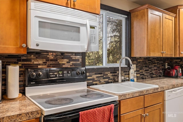 kitchen featuring a healthy amount of sunlight, tasteful backsplash, brown cabinets, a sink, and white appliances