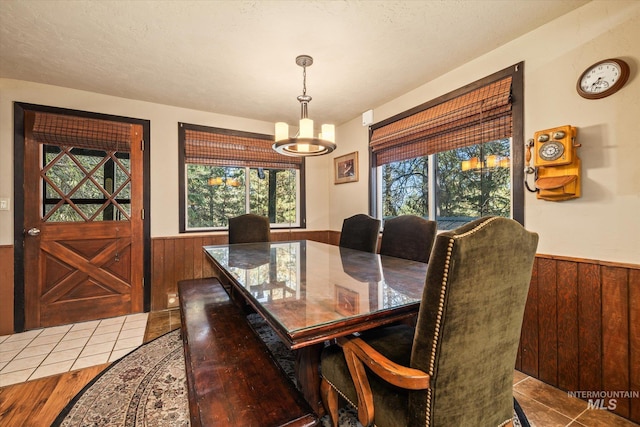 tiled dining space featuring wooden walls, a wainscoted wall, and a notable chandelier