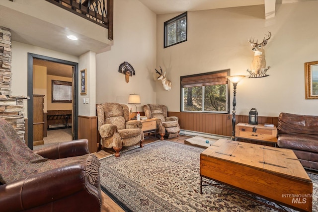 living room featuring a towering ceiling, wood finished floors, wooden walls, a wainscoted wall, and a baseboard radiator