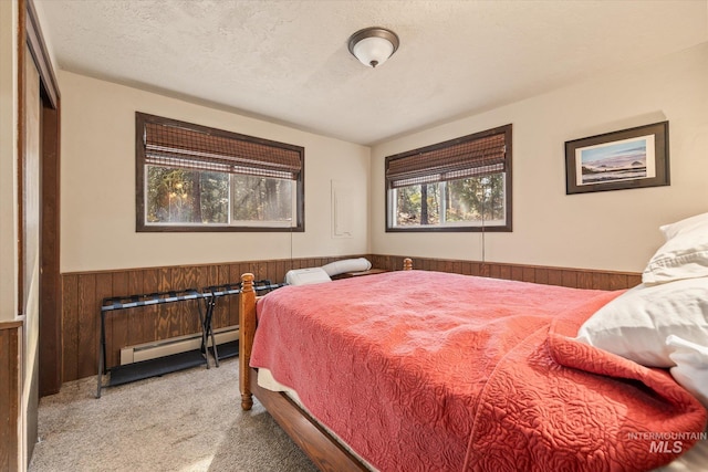 bedroom featuring a textured ceiling, a wainscoted wall, a baseboard radiator, wooden walls, and carpet