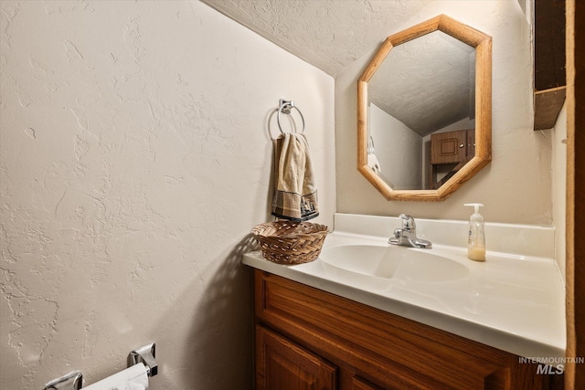 bathroom featuring vanity, a textured ceiling, a textured wall, and vaulted ceiling