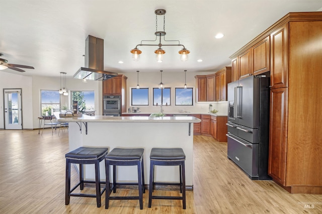 kitchen featuring a breakfast bar, high end fridge, a center island, hanging light fixtures, and island exhaust hood