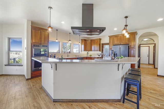 kitchen featuring a breakfast bar, island range hood, hanging light fixtures, stainless steel appliances, and a large island