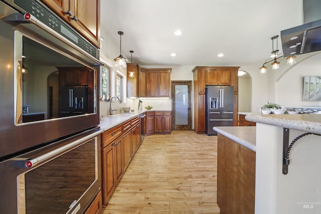 kitchen featuring hanging light fixtures, stainless steel appliances, sink, and light wood-type flooring