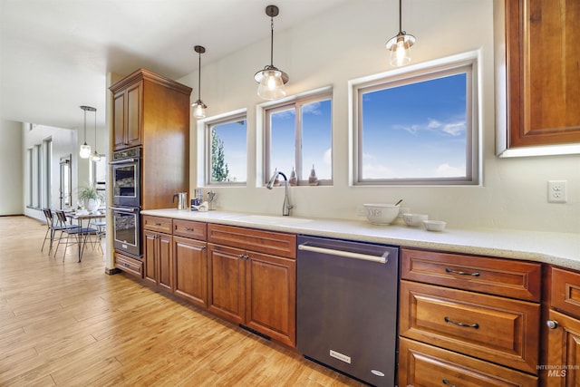 kitchen with stainless steel appliances, sink, light hardwood / wood-style floors, and decorative light fixtures