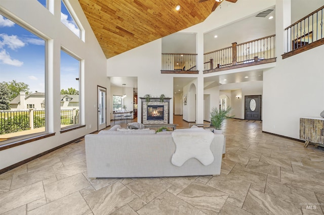 living room featuring wood ceiling, ceiling fan, a fireplace, and a towering ceiling