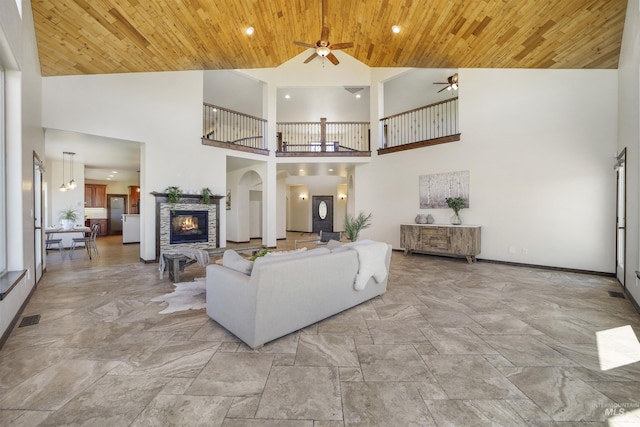 living room featuring high vaulted ceiling, a stone fireplace, wooden ceiling, and ceiling fan