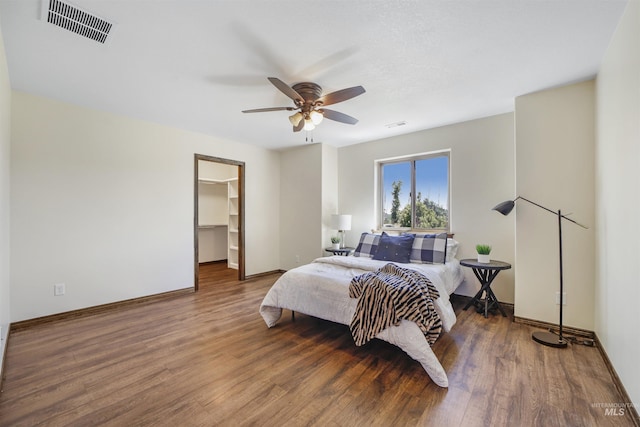 bedroom with dark hardwood / wood-style floors, ceiling fan, and a spacious closet