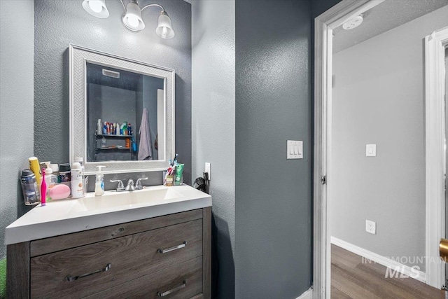 bathroom featuring a textured wall, vanity, baseboards, and wood finished floors