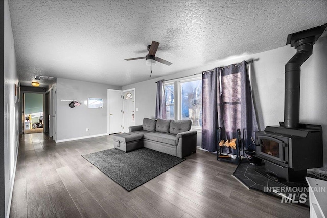 living area featuring a textured ceiling, dark wood finished floors, a wood stove, and a ceiling fan