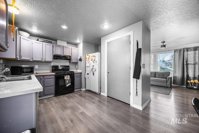 kitchen featuring white refrigerator with ice dispenser, gray cabinets, light countertops, a sink, and gas stove