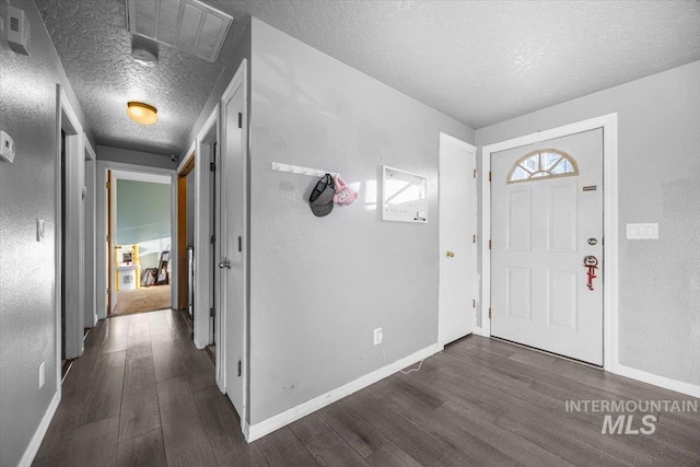 foyer featuring dark wood-style floors, a textured wall, a textured ceiling, and baseboards