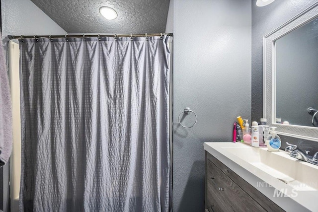 bathroom with a shower with shower curtain, vanity, a textured ceiling, and a textured wall