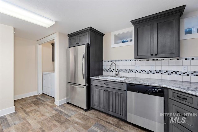 kitchen featuring light stone counters, a sink, light wood-style flooring, stainless steel appliances, and decorative backsplash