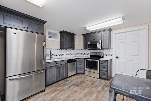 kitchen featuring decorative backsplash, appliances with stainless steel finishes, light stone countertops, a sink, and light wood finished floors