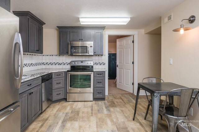 kitchen with light stone counters, gray cabinets, light wood-style flooring, stainless steel appliances, and backsplash