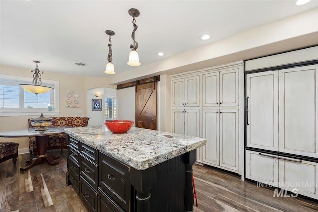 kitchen featuring a kitchen island, arched walkways, hanging light fixtures, dark cabinets, and dark wood-type flooring