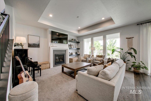 living room with a tray ceiling, recessed lighting, a glass covered fireplace, a textured ceiling, and wood finished floors