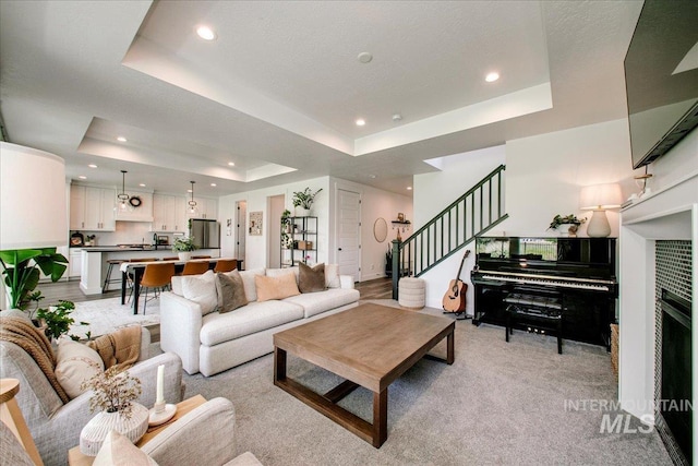 living room featuring a raised ceiling, recessed lighting, stairs, and light colored carpet
