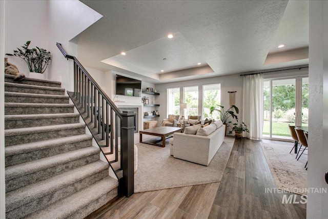 living room featuring a tray ceiling, wood finished floors, stairway, a fireplace, and recessed lighting