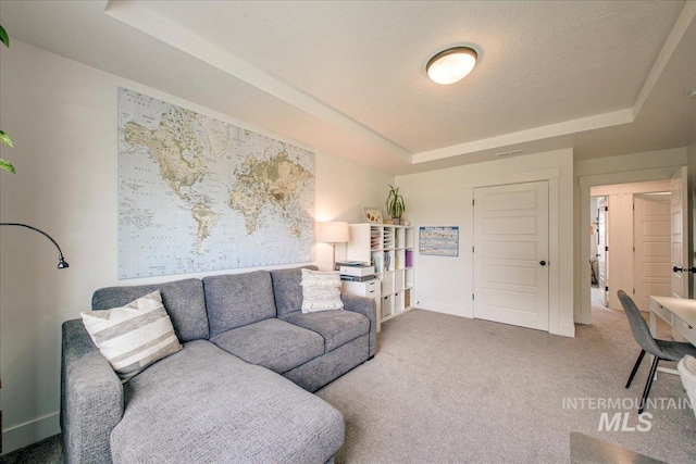 carpeted living area featuring a raised ceiling and baseboards