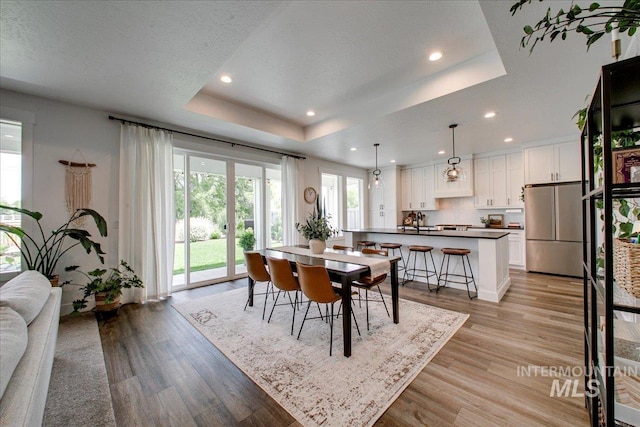 dining space featuring a raised ceiling, light wood-style floors, and recessed lighting