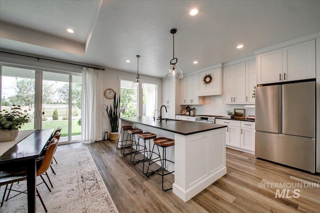 kitchen featuring stainless steel appliances, dark countertops, light wood finished floors, a kitchen breakfast bar, and white cabinetry