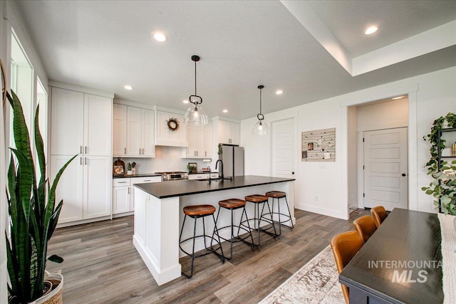 kitchen featuring dark countertops, a breakfast bar area, wood finished floors, a kitchen island with sink, and appliances with stainless steel finishes