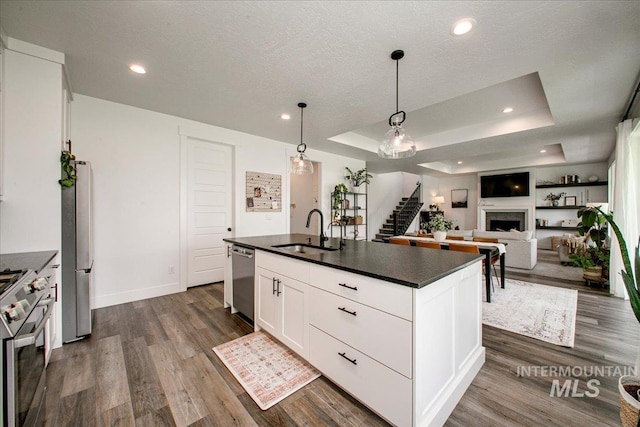 kitchen featuring a sink, appliances with stainless steel finishes, dark countertops, dark wood-style floors, and a fireplace