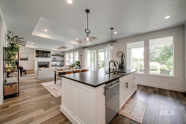 kitchen featuring a sink, dishwasher, dark countertops, a center island with sink, and white cabinets